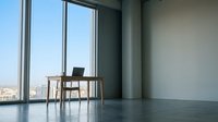 Modern minimalist office workspace with wooden desk, laptop, and chair positioned by floor-to-ceiling windows overlooking cityscape. Contemporary interior design for corporate, business, and remote work concepts.