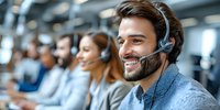 Smiling male customer service representative with headset in modern call center with diverse team in background.