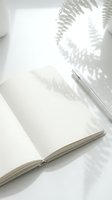 Open blank notebook with pen and fern leaf shadows on white surface, suitable for journaling, writing, planning, blogging, and creative projects.