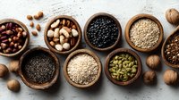 Assortment of nutritious seeds, nuts and legumes in wooden bowls on concrete background, raw organic superfoods for healthy eating.