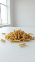Heap of uncooked spiral pasta on white surface with natural light from window, suitable for food photography, cooking blogs, recipe websites, and culinary design projects.
