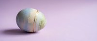 Pastel colored Easter egg with metallic gold stripes on soft purple background for spring holiday celebration and festive decoration projects.