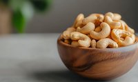 Raw cashew nuts in wooden bowl on gray concrete background with natural light and selective focus, healthy protein-rich snack for vegan diet.