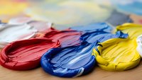 Colorful acrylic paint strokes in red blue yellow on wooden surface with blurred rainbow background for artistic creative projects and design work.