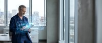 Middle-aged Caucasian businessman in suit using futuristic holographic tablet interface in modern office with city skyline view through large windows.