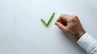 Male hand in white business shirt sleeve drawing green checkmark on white background, representing approval, confirmation and task completion.