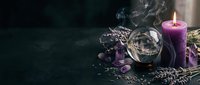 Purple candle burning with crystal ball, dried lavender flowers and mystical accessories on dark wooden surface for spiritual meditation and fortune telling.