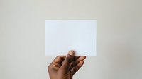 Close-up of hand holding blank white card against neutral background, suitable for mockups, presentations, and advertising campaigns.