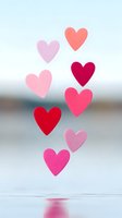 Colorful paper hearts in shades of pink and red floating against soft blue background with reflection on water surface, romantic valentines day concept.