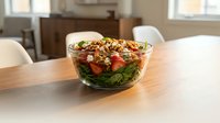 Fresh spinach salad with strawberries, walnuts, and feta cheese in a glass bowl on a wooden dining table in a bright home interior.
