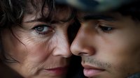 Close-up portrait of young Hispanic man and mature Caucasian woman faces in intimate emotional moment against dark background showing connection and relationship.