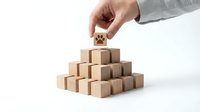 Hand placing wooden cube on pyramid of blocks representing business growth, teamwork and strategic planning concepts on white background.