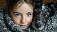Young Caucasian girl with blue eyes cuddling adorable gray and white puppy dog in cozy knit blanket. Heartwarming pet adoption and childhood friendship concept.