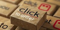 Macro view of cardboard box with click to order text, highlighting online shopping and e-commerce concept against blurred background of similar boxes.
