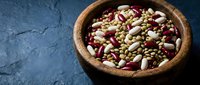 Mixed legumes and beans variety in wooden bowl on dark textured background for healthy cooking and nutrition concepts.
