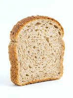 Slice of whole wheat bread with golden crust and soft interior crumb structure, isolated on white background for bakery, food, and culinary design projects.