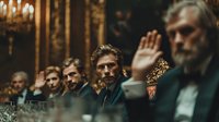 Middle-aged Caucasian man raising hand during formal meeting in ornate boardroom with colleagues seated around table in corporate business setting.