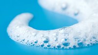 White foam bubbles floating on bright blue water surface creating abstract aquatic texture for spa wellness and cleaning product designs.