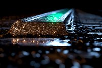 Glowing green light emerges from open book pages covered in water droplets, creating magical atmosphere with sparkles and reflections in dark setting.