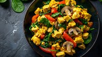 Colorful tofu scramble with mushrooms, red peppers and spinach served on dark plate. Healthy vegan protein meal with turmeric and vegetables.