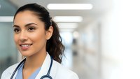 Young female doctor with stethoscope smiling confidently in modern hospital corridor. Professional healthcare worker portrait for medical marketing.