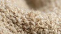 Close-up macro shot of beige knitted wool fabric texture showing detailed cable knit pattern and natural fiber structure for cozy winter fashion designs.