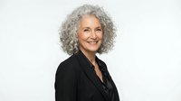 Professional mature woman with curly gray hair smiling confidently in black blazer on white background for business and corporate marketing materials.