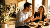 Young couple enjoying romantic dinner date at cozy restaurant with warm lighting, sharing meal and conversation in intimate dining setting.