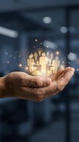 Businessman hand holding glowing golden human figures with sparkling light effects against blurred office background, representing team building, leadership, human resources, and workforce management.