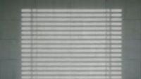Venetian blind shadow pattern cast on white wall creating geometric striped light and dark lines for interior design and architectural backgrounds.