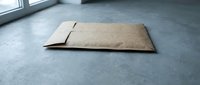 Flat cardboard box packaging lying on concrete floor near window with natural light for shipping and delivery services.
