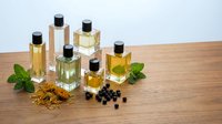 Collection of elegant glass perfume bottles with golden fragrance on wooden surface, surrounded by mint, dried flowers, and berries.
