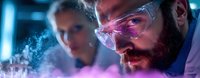 Bearded male scientist in protective eyewear examining glowing experiment with purple smoke while female researcher observes in modern laboratory setting.