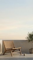 Wooden lounge chair with woven rattan seat on minimalist terrace at sunset, featuring potted olive plant and ceramic cup for relaxation and outdoor living spaces.