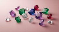 Collection of colorful precious gemstones including diamonds, emeralds, sapphires and rubies scattered on pink background for jewelry design.