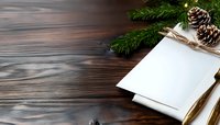 Blank white paper with pine branches and cones on dark wooden background. Christmas mockup for greeting cards and winter holiday designs on rustic table surface.