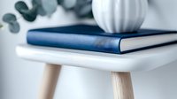 Minimalist home decor arrangement with navy blue hardcover book and white ceramic vase on modern scandinavian style side table with eucalyptus leaves.