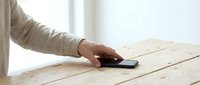 Male hand with dark skin tone using smartphone on wooden table surface, casual technology interaction and mobile device usage.