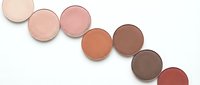 Cosmetic eyeshadow palette with neutral brown and pink tones arranged in curved line on white background for makeup and beauty applications.