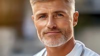 Confident mature Caucasian man with gray beard and styled hair wearing white shirt smiling at camera, natural lighting creates warm atmosphere for business portrait.