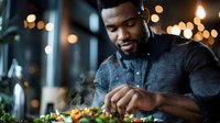 African American male chef carefully garnishing gourmet dish in upscale restaurant with warm ambient lighting and bokeh background.