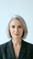 Mature woman with gray hair wearing dark blazer against white background, professional headshot for corporate business portraits and executive profiles.