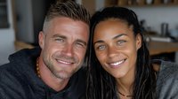Smiling interracial couple relaxing together at home on couch, happy mixed race partners embracing in cozy living room interior for lifestyle content.