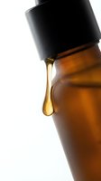 Amber glass dropper bottle with golden liquid dripping from black cap, isolated on white background for cosmetics, essential oils, serums, and skincare product packaging design.