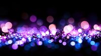 Magical purple and blue bokeh lights creating dreamy abstract background with glowing particles and blurred circles on black surface, festive atmosphere.