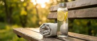 Refreshing lemon water with fresh citrus slices in glass bottle on wooden bench with rolled towel, outdoor wellness and hydration concept for summer relaxation.