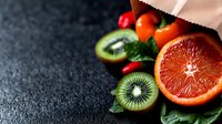 Fresh grapefruit and kiwi slices spilling from cloth bag onto dark surface, colorful tropical fruits for healthy eating, nutrition and wellness content.