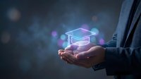 Professional businessman holding glowing graduation cap hologram representing online education, e-learning technology and academic achievement in digital era.