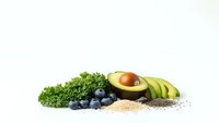 Fresh superfood ingredients including kale, blueberries, avocado and quinoa seeds arranged on white background for healthy eating and nutrition concepts.