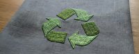 Green recycling symbol embroidered on gray fabric surface. Eco-friendly sustainability concept for environmental awareness campaigns and green living materials.